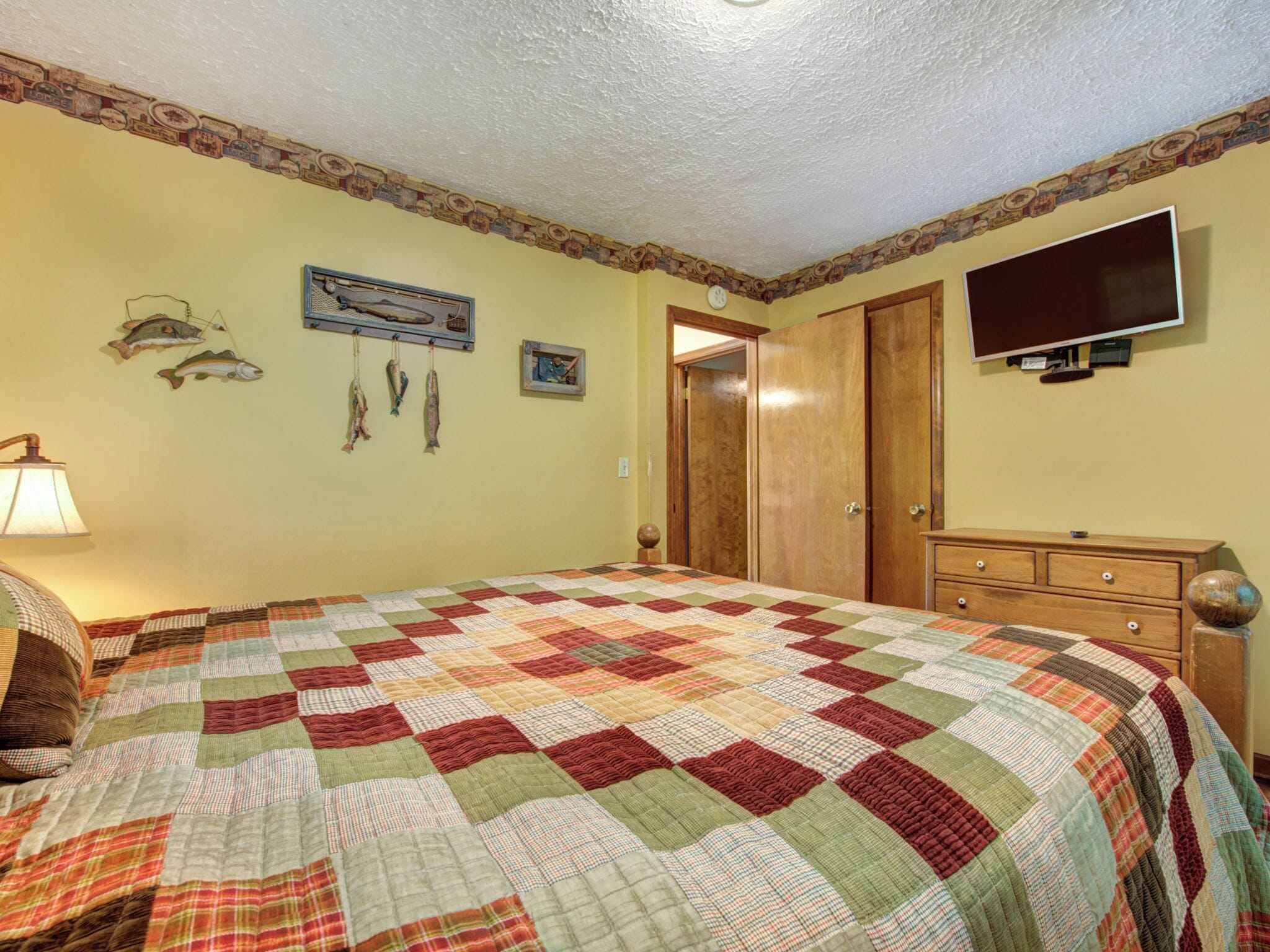 Ein Schlafzimmer mit einem großen Bett, einem Schminktisch, einem an der Wand befestigten Fernseher und einer Tür zu einem anderen Raum.