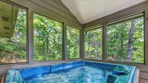 A hot tub with a view of a forest through large windows. - Mountain Charm by Jackson Mountain Rentals (Gatlinburg)
