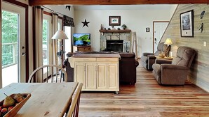 A cozy living room with a wooden dining table, a sofa, and a TV. - Mountain Charm by Jackson Mountain Rentals (Gatlinburg)