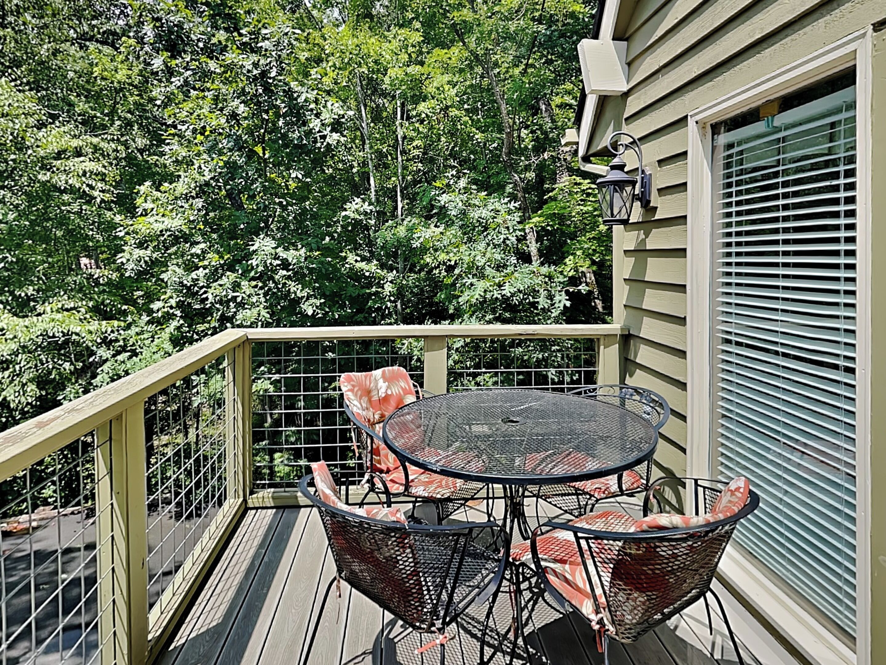 A wooden deck with a round table and four chairs, surrounded by a metal railing.