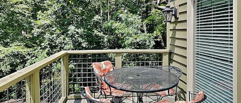 Eine Holzdielen-Terrasse mit einem runden Tisch und vier Stühlen, umgeben von einem Metallgeländer.