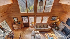 A spacious wooden cabin with a high ceiling, large windows, a cozy living area with a sofa and coffee table, a fireplace, and a dining area with a wooden table and chairs. - Mountain Treasure by Jackson Mountain Rentals (Gatlinburg)