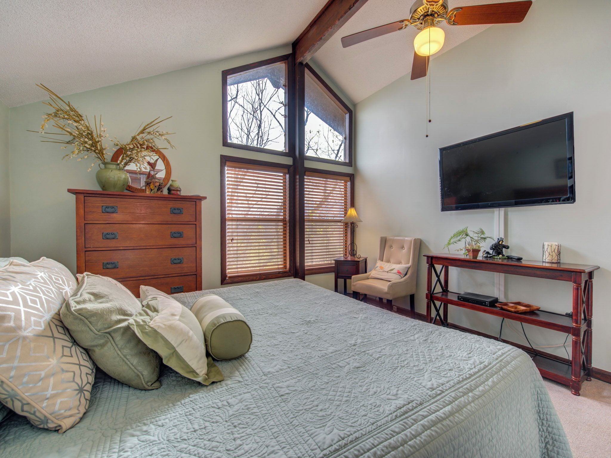 A bedroom with a large bed, a dresser, a television, and a desk.