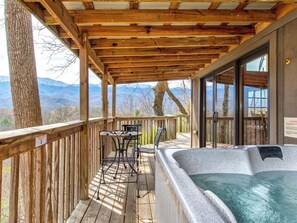 A wooden deck with a hot tub, a table, and chairs, overlooking a mountainous landscape. - Mountain Treasure by Jackson Mountain Rentals (Gatlinburg)