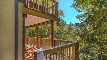A wooden deck with a railing, a covered area, and a view of trees and mountains.