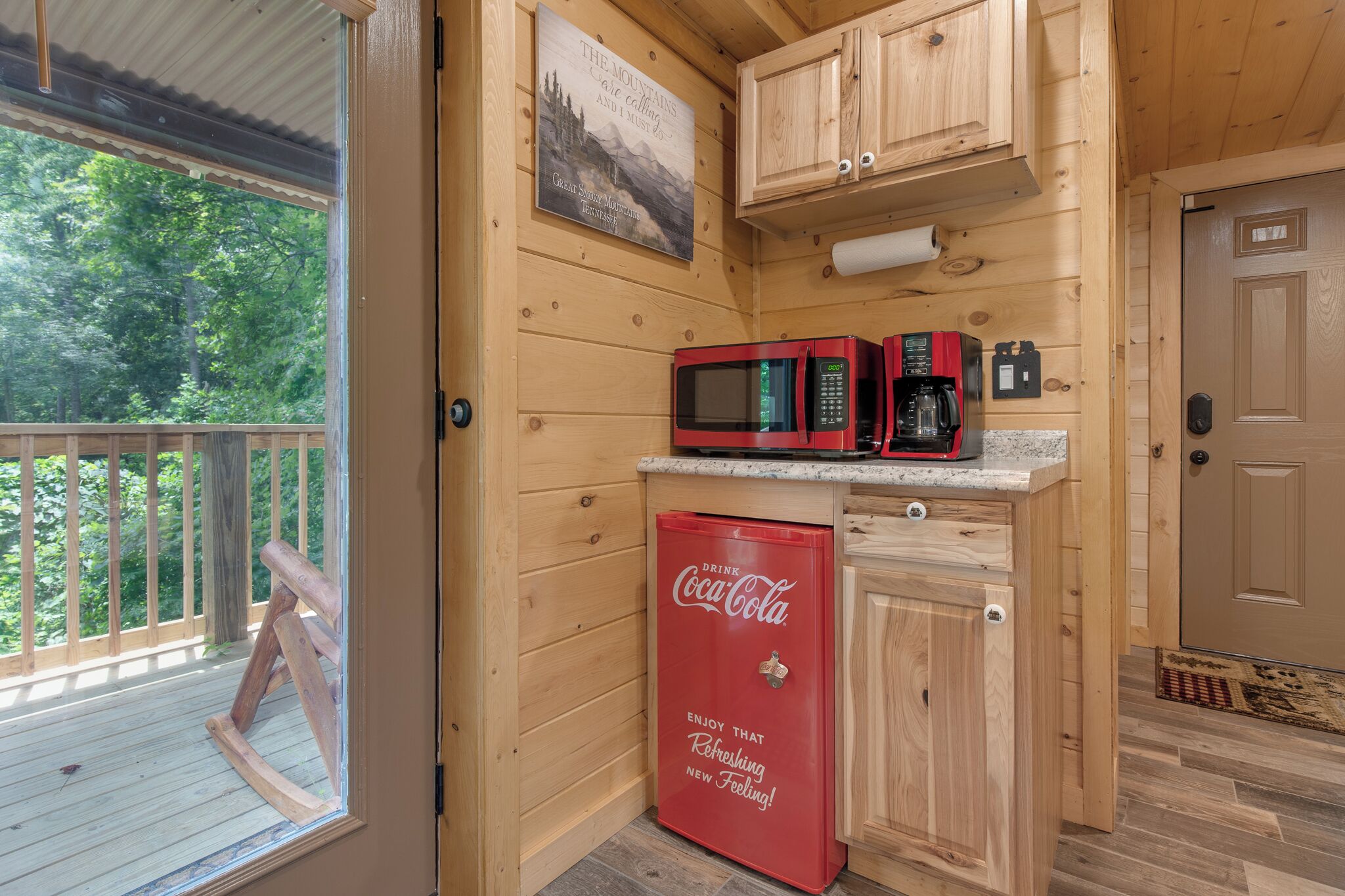 A compact kitchen with wooden cabinetry, a microwave, a coffee maker, and a Coca-Cola refrigerator.