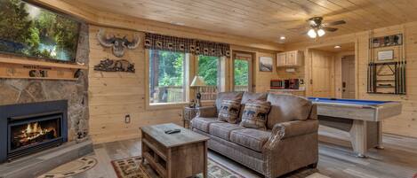 A cozy cabin interior with a fireplace, a pool table, and a comfortable seating area.