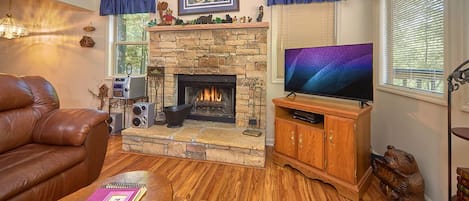 A cozy living room with a stone fireplace, leather sofa, and a television on a wooden stand.
