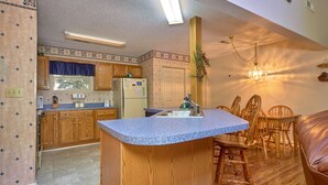 A compact kitchen with wooden cabinets, a granite countertop, and a dining area with wooden chairs and a table. - Mountain Hideaway by Jackson Mountain Rentals (Gatlinburg)