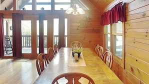 Ein Esszimmer mit Holzboden, einem langen Tisch und Stühlen, großen Fenstern und einem Deckenventilator.