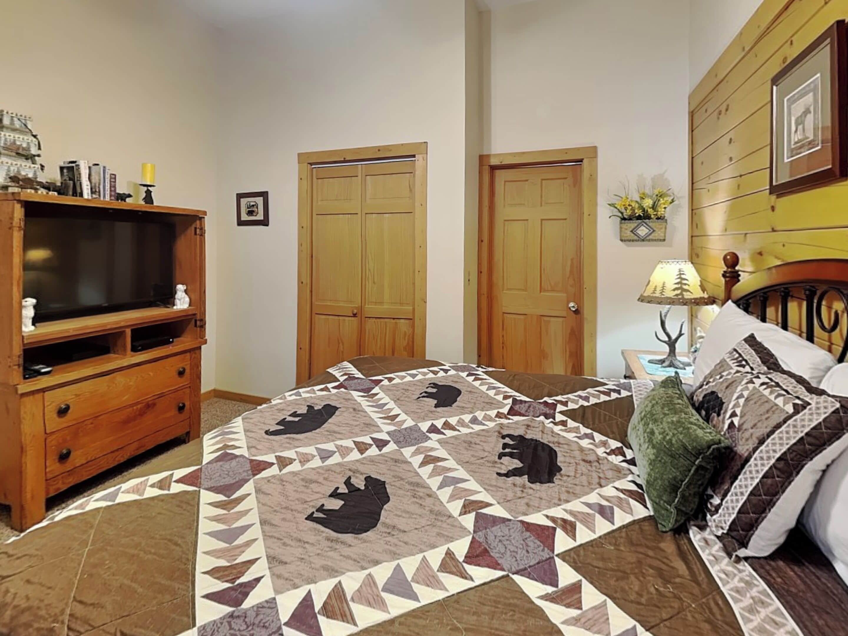 A bedroom with a large bed, a wooden dresser, a television, and two doors.