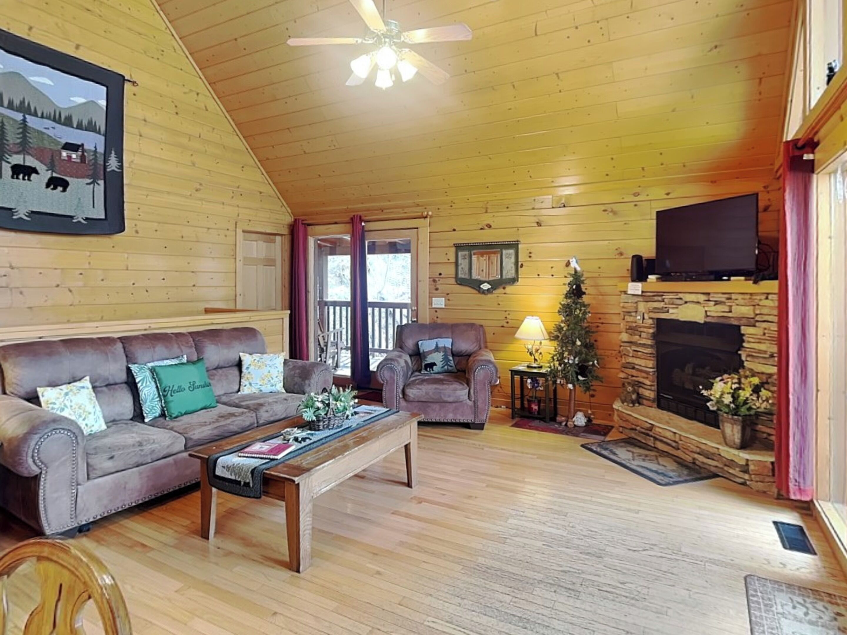 L’intérieur d’une cabane en rondins, avec une cheminée, un téléviseur, un ventilateur de plafond et un tableau encadré au mur.