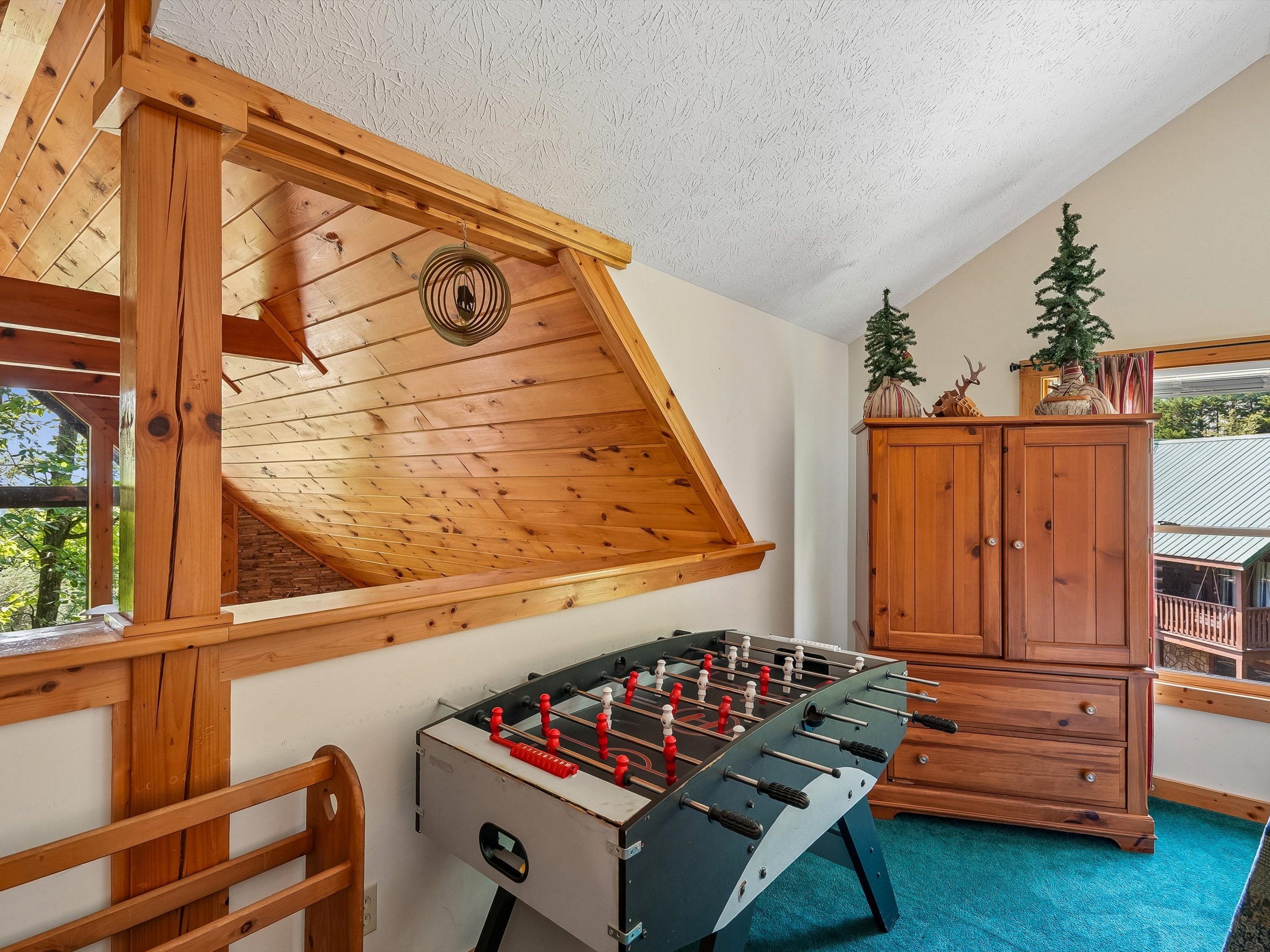 Una habitación con techo de madera, mesa de fútbol de mesa, un armario y un pequeño árbol de Navidad.
