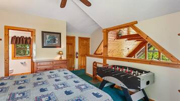 A bedroom with a bed, a wooden ceiling fan, a window with a view, and a foosball table.