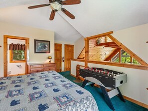 Quarto com cama, ventilador de teto em madeira, janela com vista e mesa de futebol.