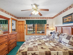 A bedroom with a bed, a ceiling fan, a window with a view, a dresser, and a lamp. - Komfy Kozy by Jackson Mountain Rentals (Gatlinburg)