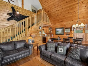 A wooden interior with a staircase, leather sofas, a dining area, and a mounted animal head. - Komfy Kozy by Jackson Mountain Rentals (Gatlinburg)