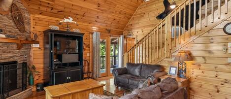 A wooden interior with a fireplace, leather sofa, and a staircase.