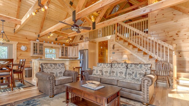 Un intérieur spacieux de chalet en bois, comprenant un salon, une cuisine et un escalier.