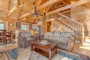 Cozy cabin-style home features a spacious living area with a sofa set, dining table, and staircase leading to an upper level.