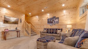 L’intérieur d’une cabane en rondins, avec un escalier, un ensemble de canapés et un tableau représentant des loups.