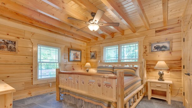 Ein Schlafzimmer einer Holzhütte mit einem Bett, zwei Fenstern, einem Deckenventilator und einem Nachttisch mit Lampe.