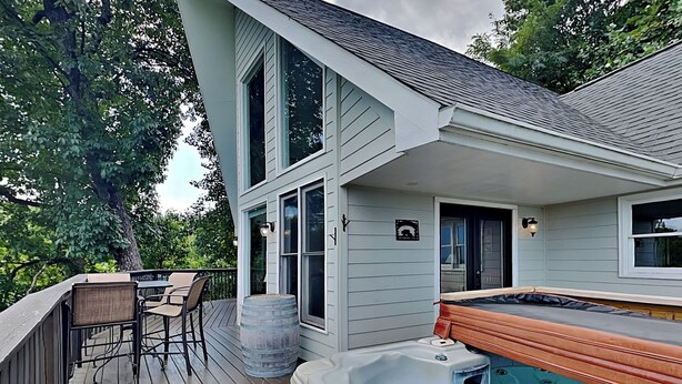 A deck with a hot tub, a table with chairs, and a large tree in the background. - Kickback Kabin by Jackson Mountain Rentals (Gatlinburg)