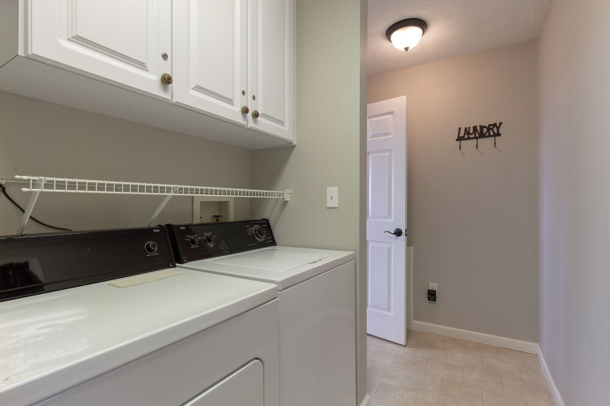 A laundry area with a white washer and dryer, a white shelf, and a door labeled "LAUNDRY".