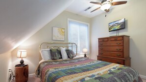 A bedroom with a bed, a dresser, a ceiling fan, a wall-mounted TV, and a window with blinds. - Kickback Kabin by Jackson Mountain Rentals (Gatlinburg)