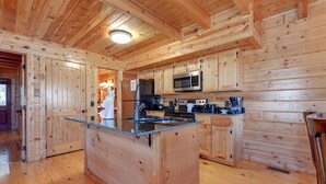 Eine Holzhütte-Küche mit einer zentralen Kochinsel, Holzschränken und einem Edelstahl-Kühlschrank.