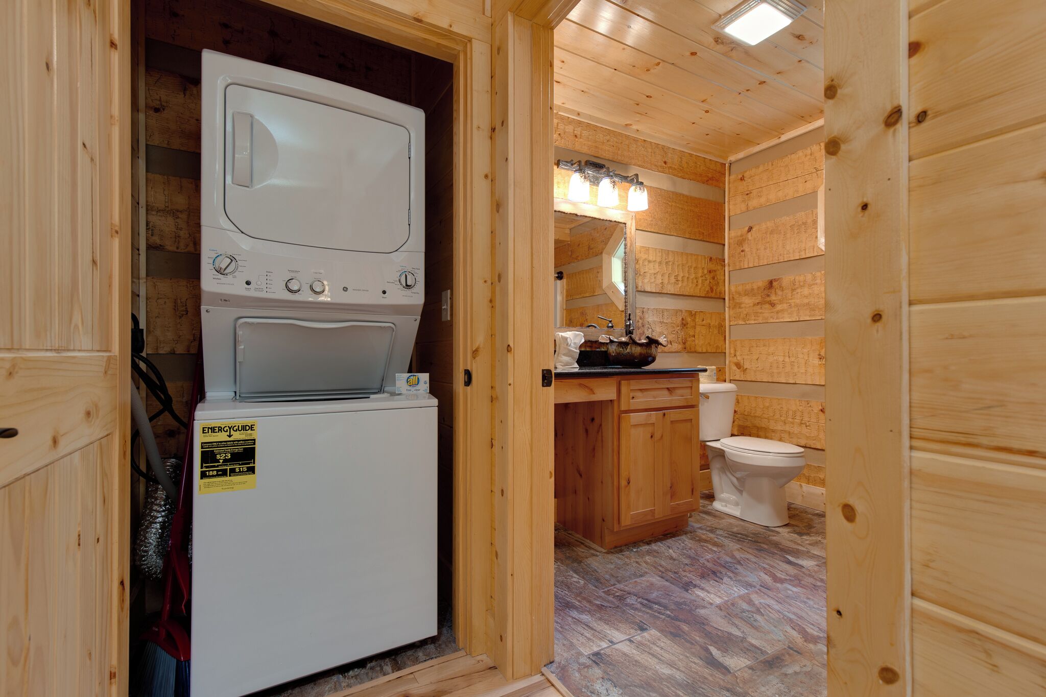 A compact wooden bathroom with a washing machine, a toilet, and a sink.