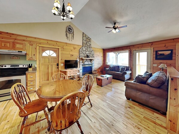 Cozy cabin-style room with a dining table, sofa, and fireplace.