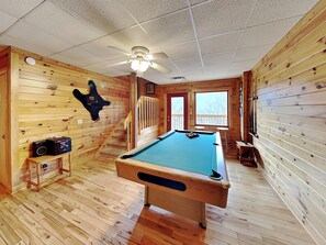 Enjoy a game of pool in this spacious room with a pool table, staircase, and window offering a view of the outside.