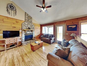 Cozy cabin with a fireplace, sofa, and large window offering a forest view.