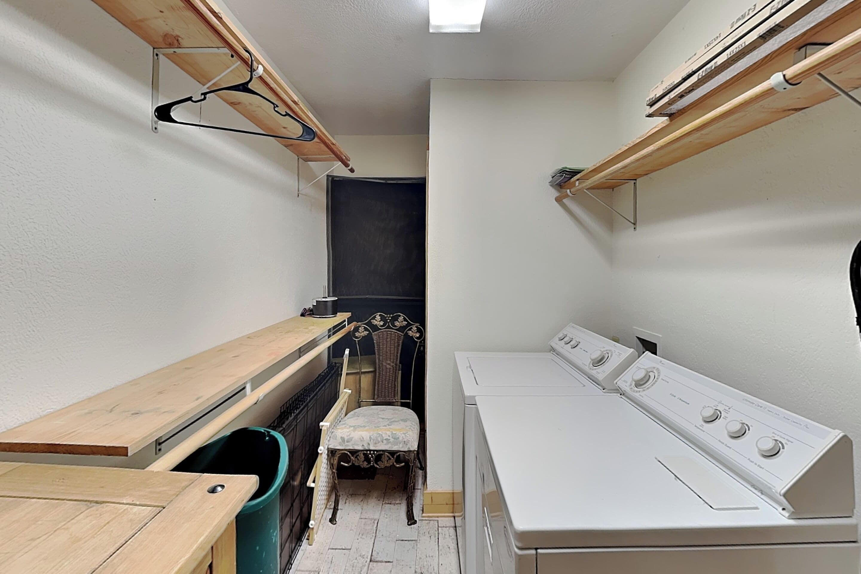 A laundry room with a washing machine, a drying rack, a chair, and a trash bin.