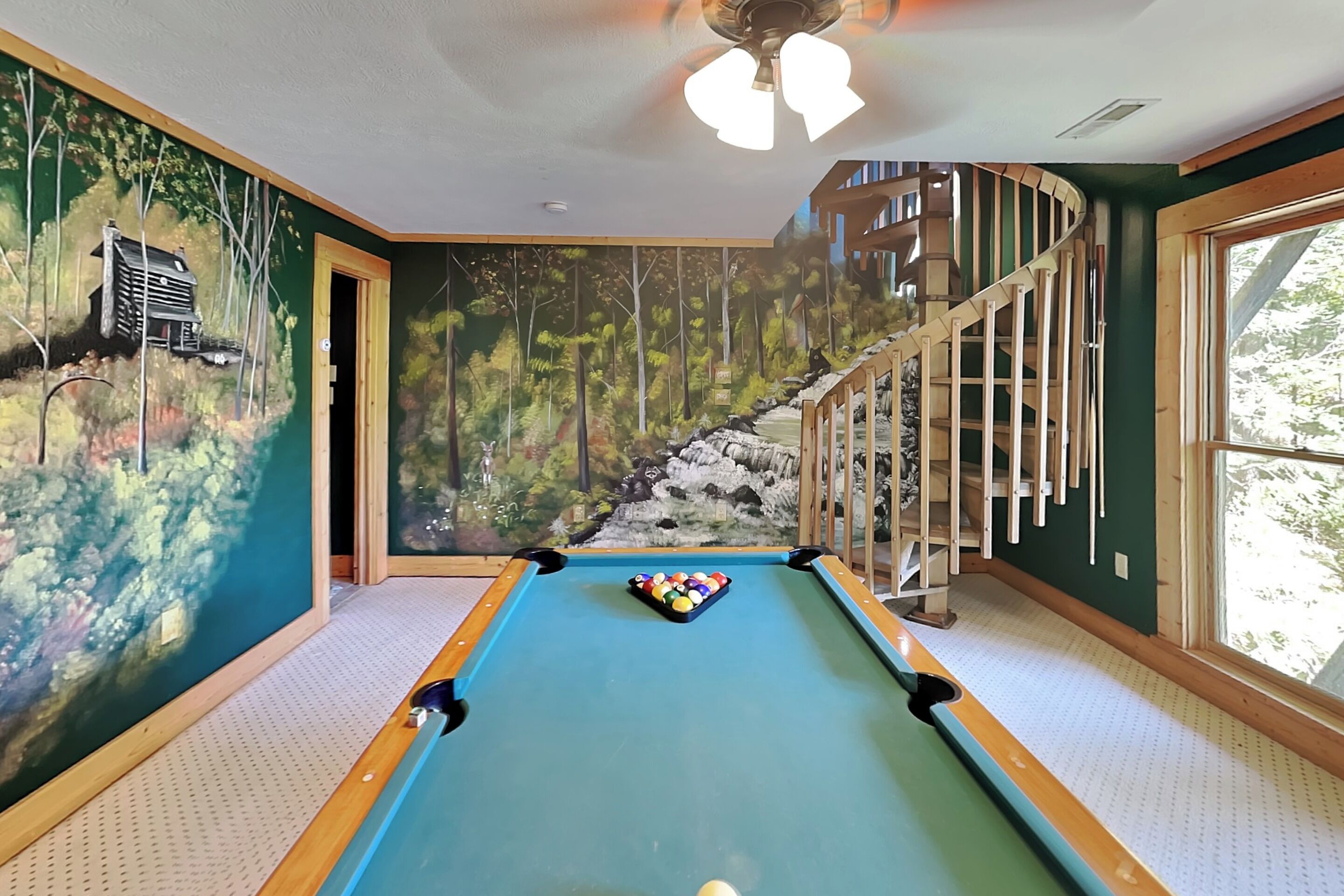 A pool table with a mural of a forest and a staircase.