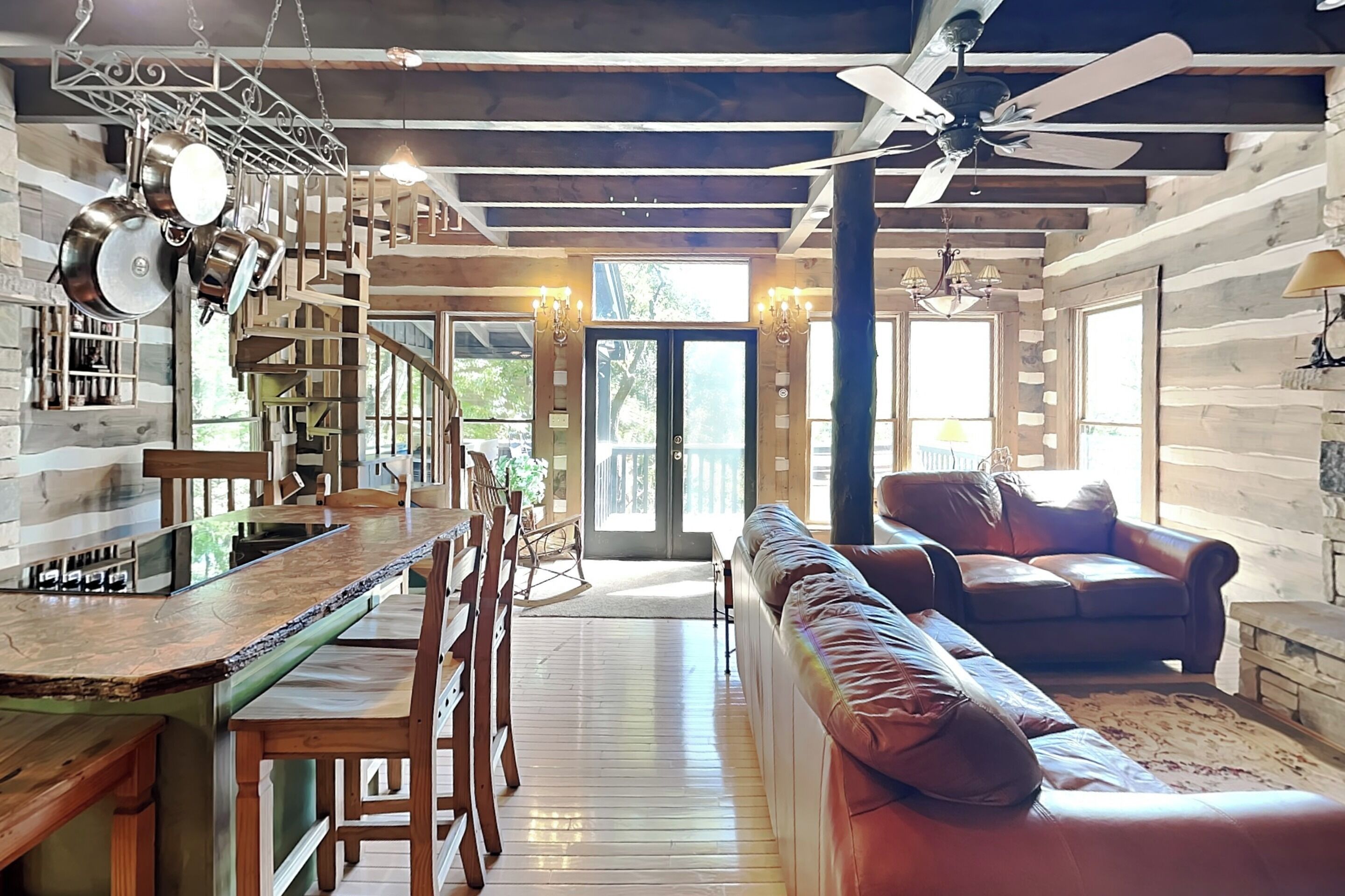 Un interior espacioso con una escalera de madera, un comedor, una zona de estar con sofá y un ventilador de techo.