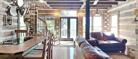 Un interior espacioso con una escalera de madera, un comedor, una zona de estar con sofá y un ventilador de techo.