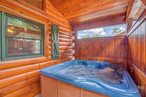 A wooden cabin with a hot tub, wooden walls, and a window with green shutters.