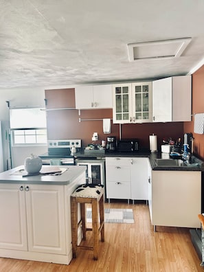 A compact kitchen with white cabinets, a wooden countertop, and a small dining area with a stool. - Cozy creative getaway  guesthouse (Safety Harbor)