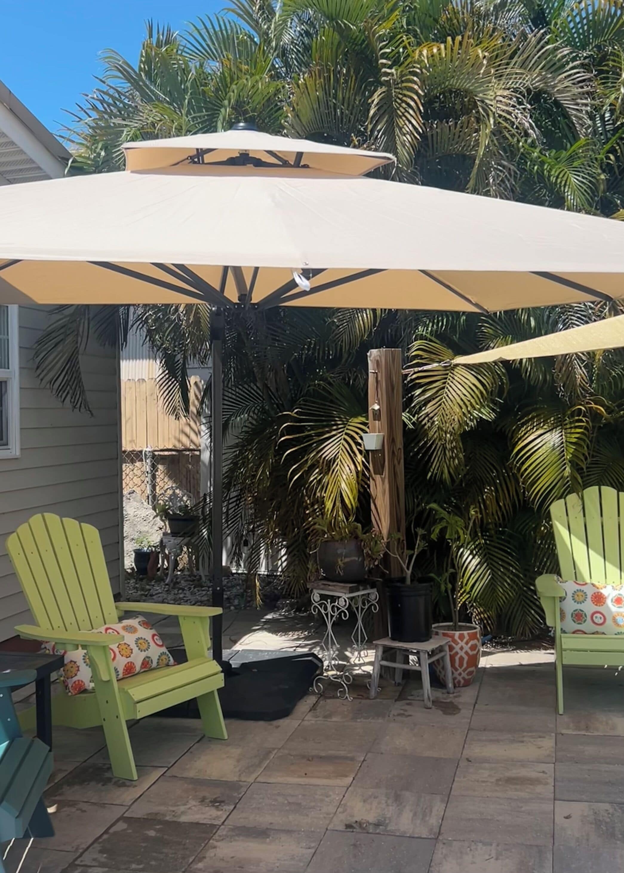 Un patio con un par de sillones Adirondack verdes, una mesa pequeña y una sombrilla grande.