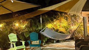 Un espace extérieur aménagé avec une terrasse, un hamac, deux fauteuils Adirondack et un coin salon abrité.