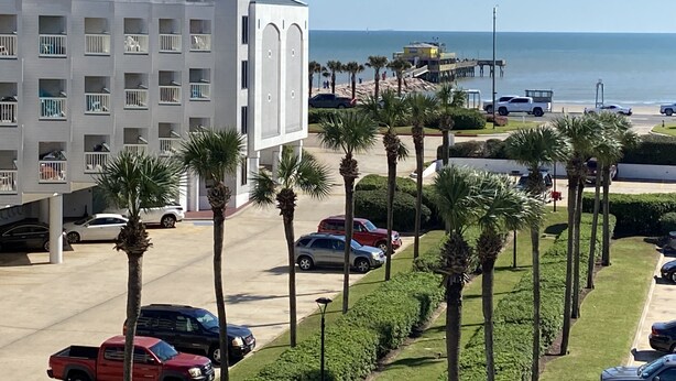 Een hotel met een modern design, met een parkeerplaats vol auto's, palmbomen en uitzicht op de oceaan.
