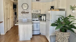 Een moderne keuken met witte kastjes, een ingebouwde oven en een koelkast. Een klok hangt aan de muur, en er staat een welkomstbord.