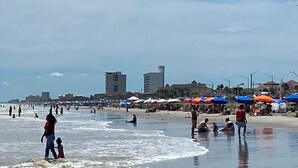 Een strand met mensen, parasols en gebouwen op de achtergrond.