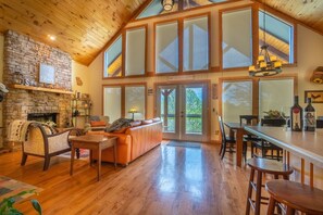 Amplia sala de estar con chimenea de piedra, un sofá grande y una mesa de comedor de madera.