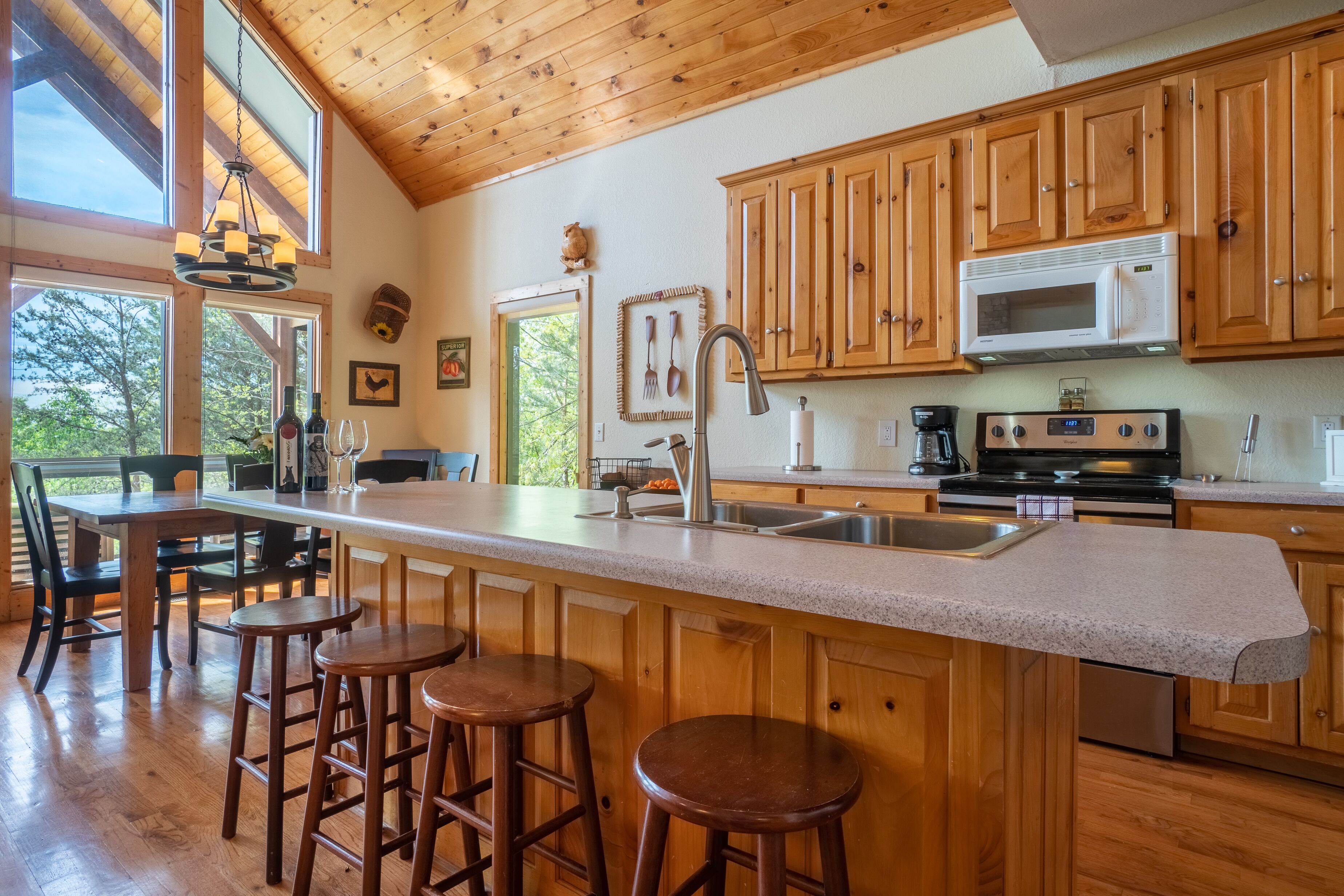 A kitchen with wooden cabinets, a large island with stools, a microwave, and a stove.