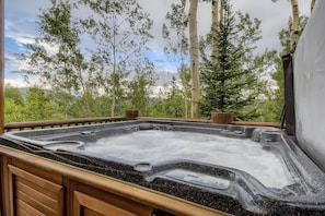 A hot tub with a wooden deck and a view of trees and sky.