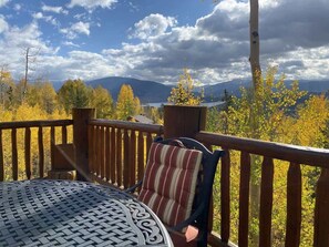 A wooden deck with a table and chairs, overlooking a mountainous landscape.