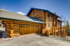 Eine Blockhütte mit Garage, überdachter Veranda und einer Treppe zum Haupteingang.